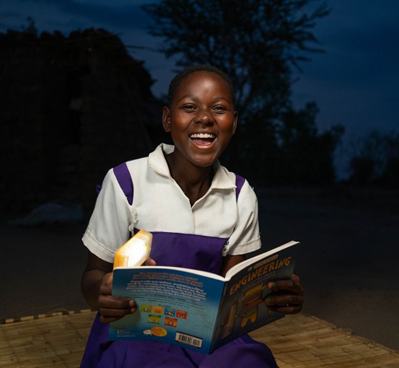 Girl looking into the camera smiling, holding a book